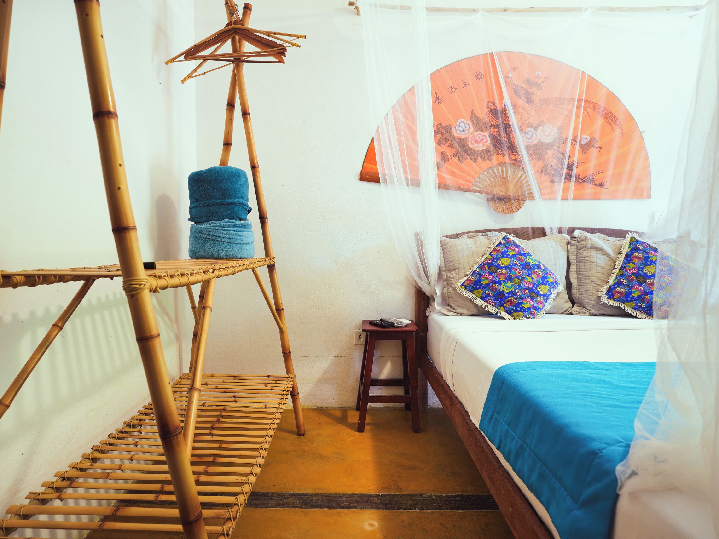 A room with a bed, a bamboo shelf, a small table, and a decorative fan.
