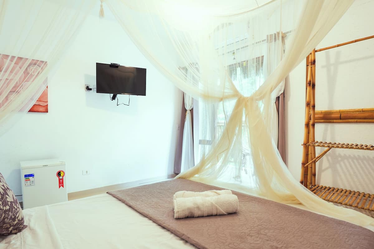 Ein Schlafzimmer mit Bett, Fernseher und Moskitonetz.