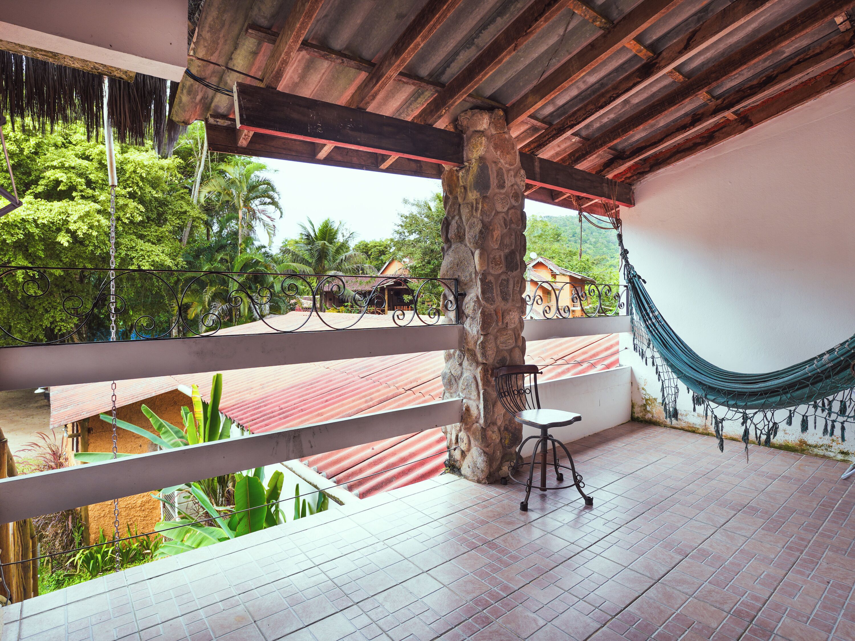 A balcony with a hammock, a chair, and a view of a red-roofed building and greenery.