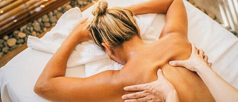 A person receiving a back massage on a white massage table in a room with a wooden floor.