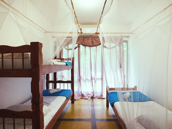 Una habitación con dos literas de madera, una mosquitera y una ventana con cortinas traslúcidas.