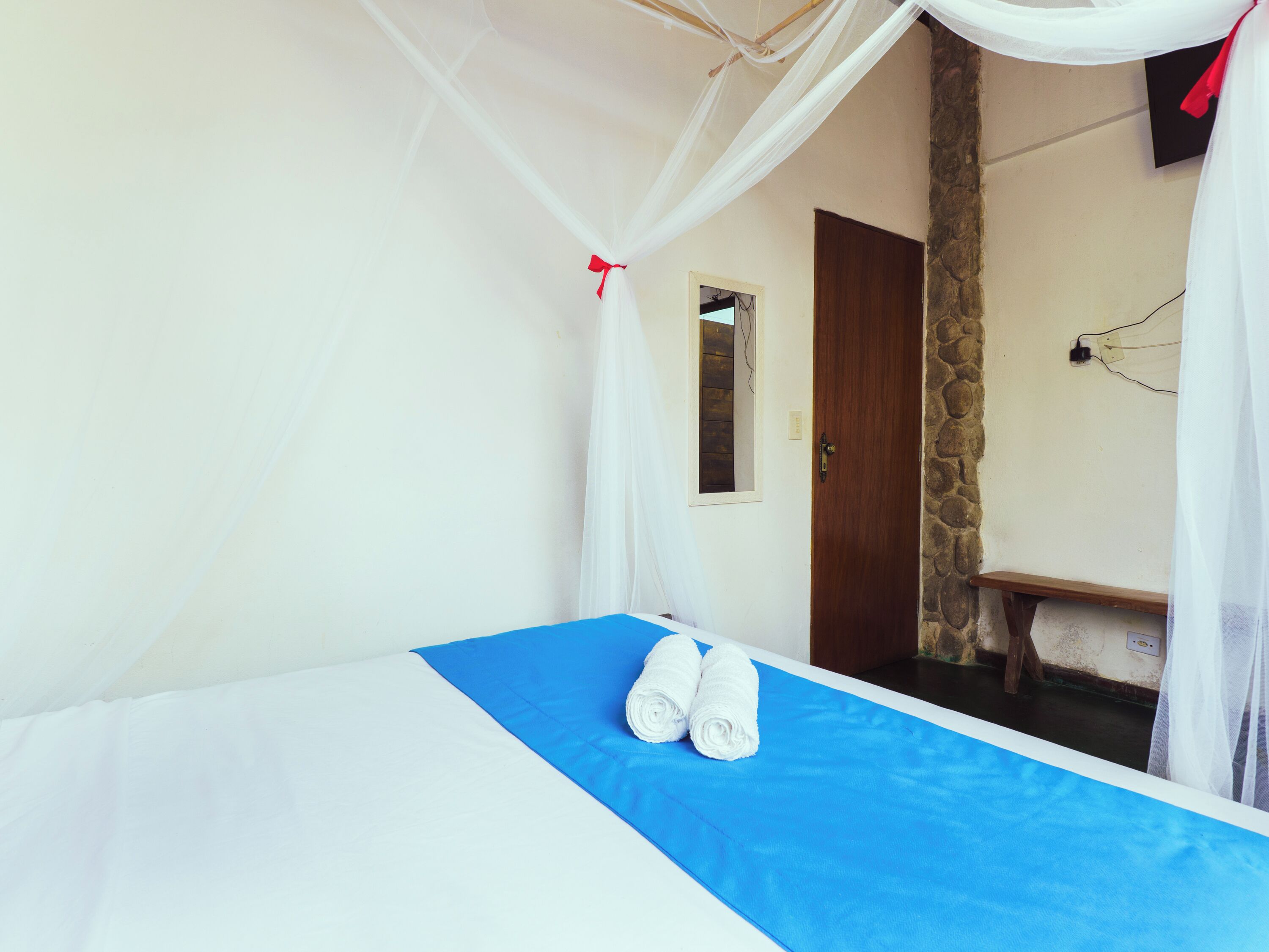 A room with a bed, a bench, a door, and a stone wall.