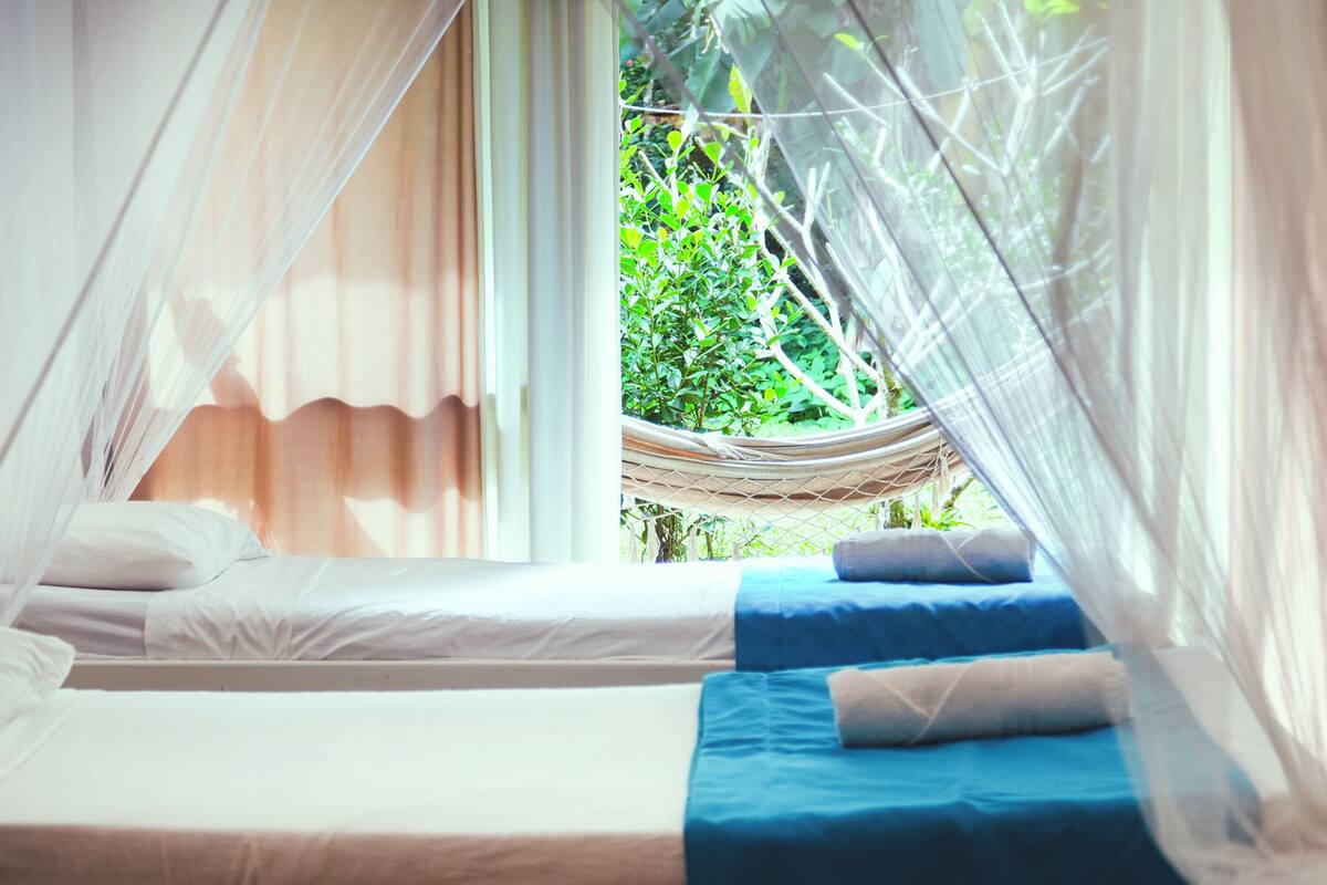 Ein Schlafzimmer mit zwei Betten, einer Hängematte und Blick auf grüne Vegetation.