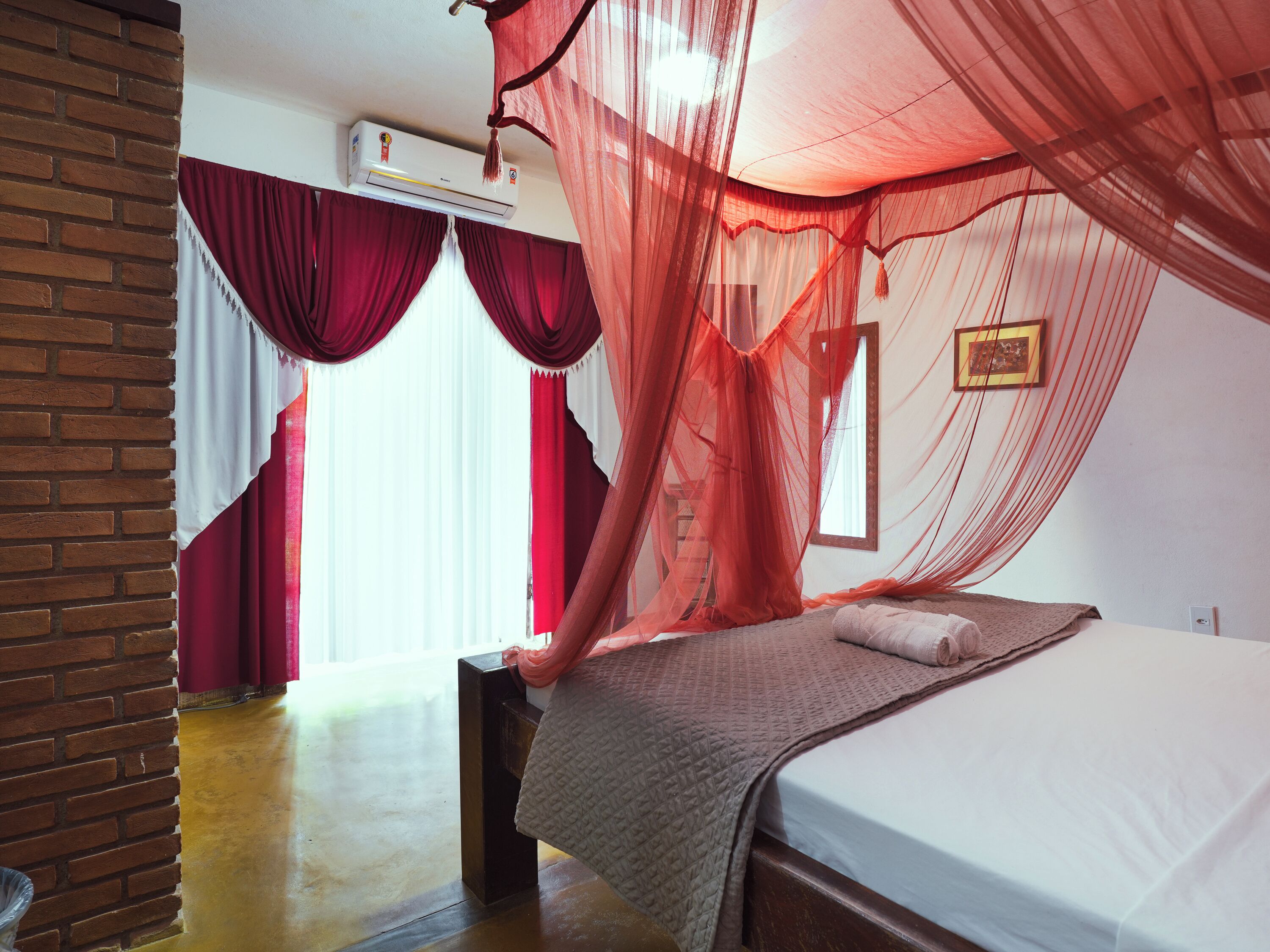 A bedroom with a bed, a mosquito net, and a brick wall.