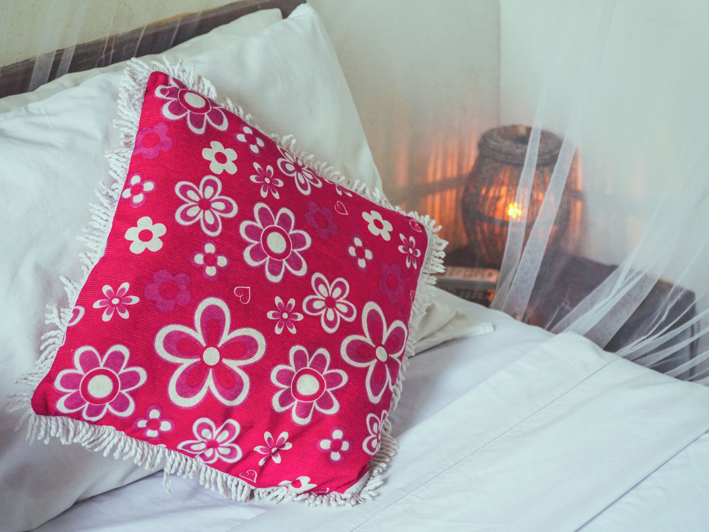 Una cama con ropa de cama blanca y una almohada con estampado floral rojo.