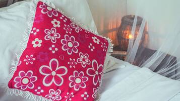 Una cama con ropa de cama blanca y una almohada con estampado floral rojo.