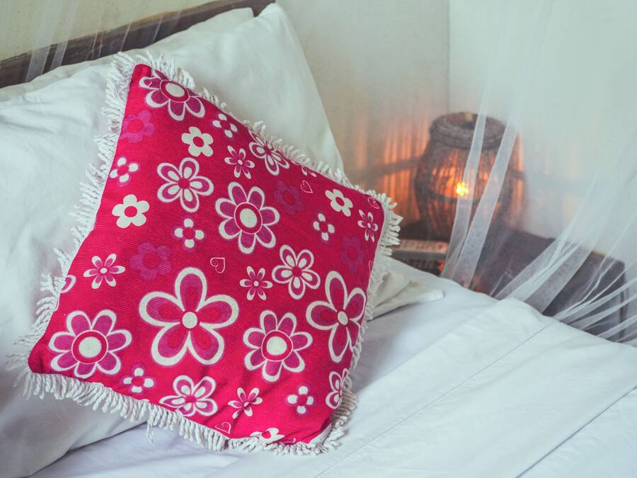 Una cama con ropa de cama blanca y una almohada con estampado floral rojo.