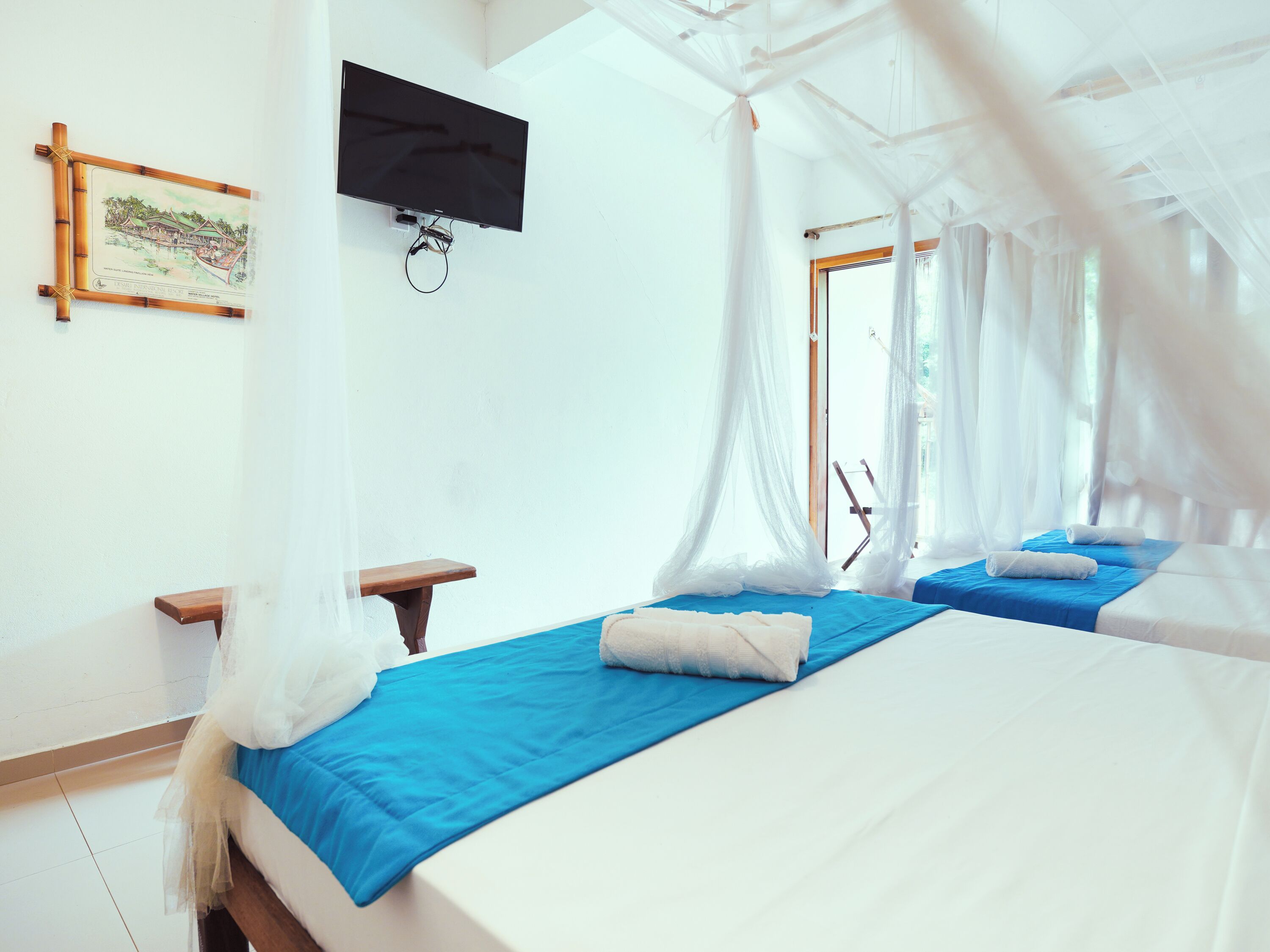 Un dormitorio con dos camas, un televisor montado en la pared y una ventana con cortinas translúcidas.