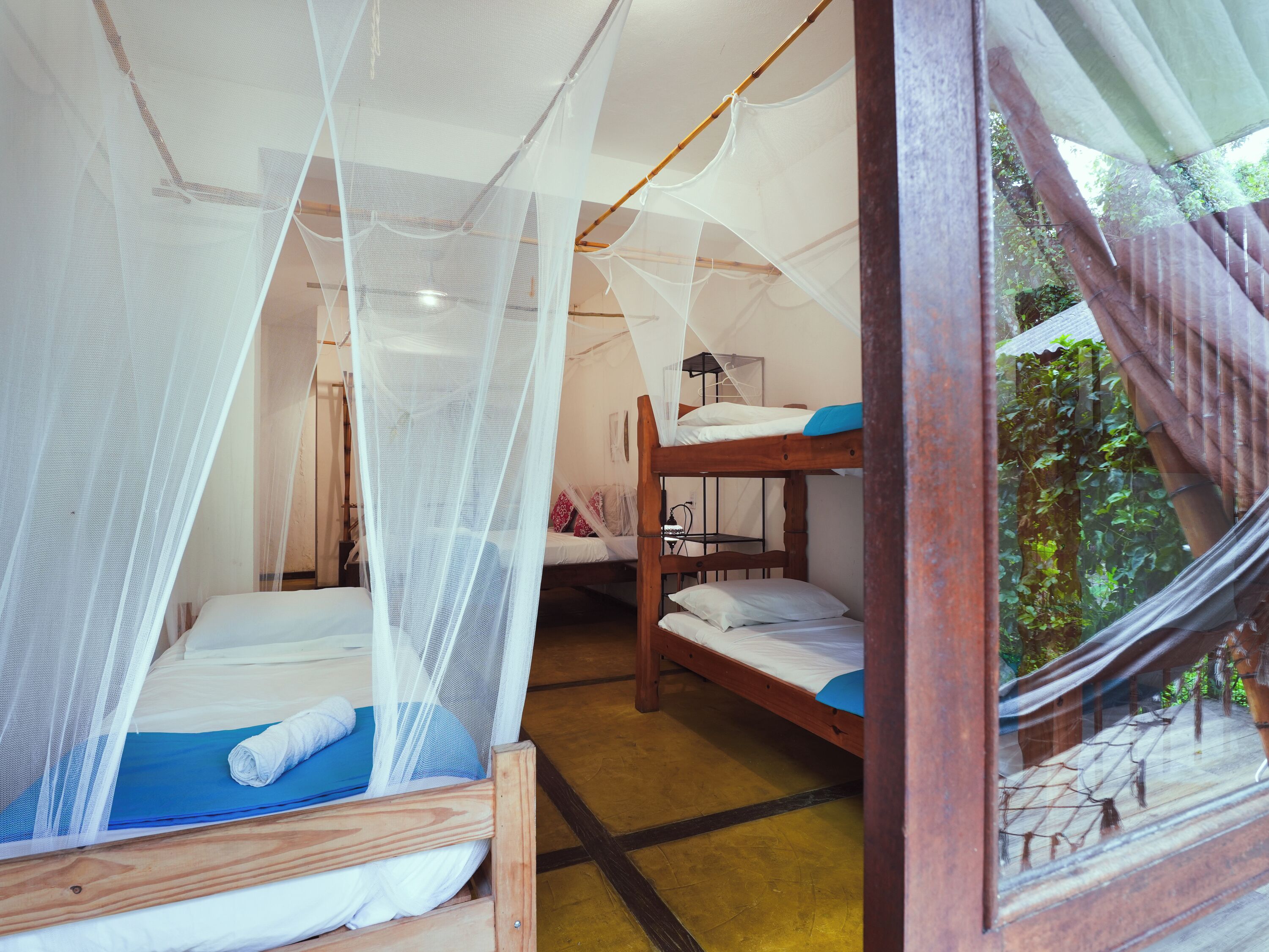 Een kamer met een bed onder een klamboe, een stapelbed en een raam met uitzicht op groen.
