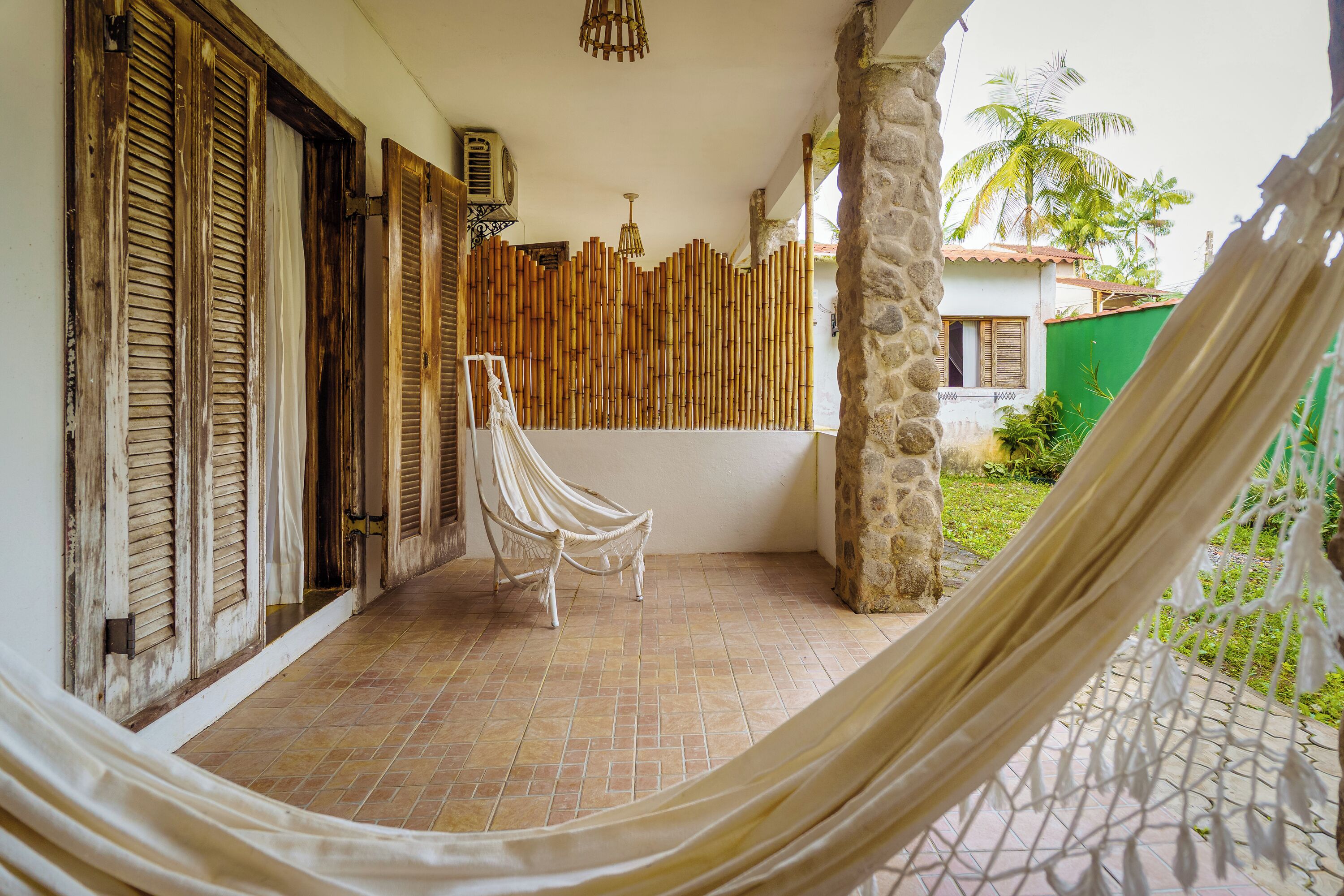 A hammock on a tiled patio with a bamboo wall and a white chair.