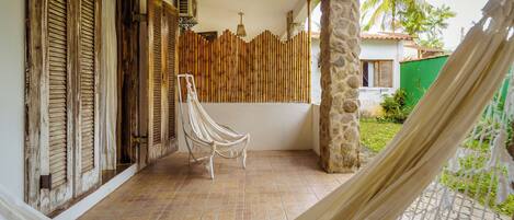Una hamaca en un patio empedrado con un muro de bambú y una silla blanca.
