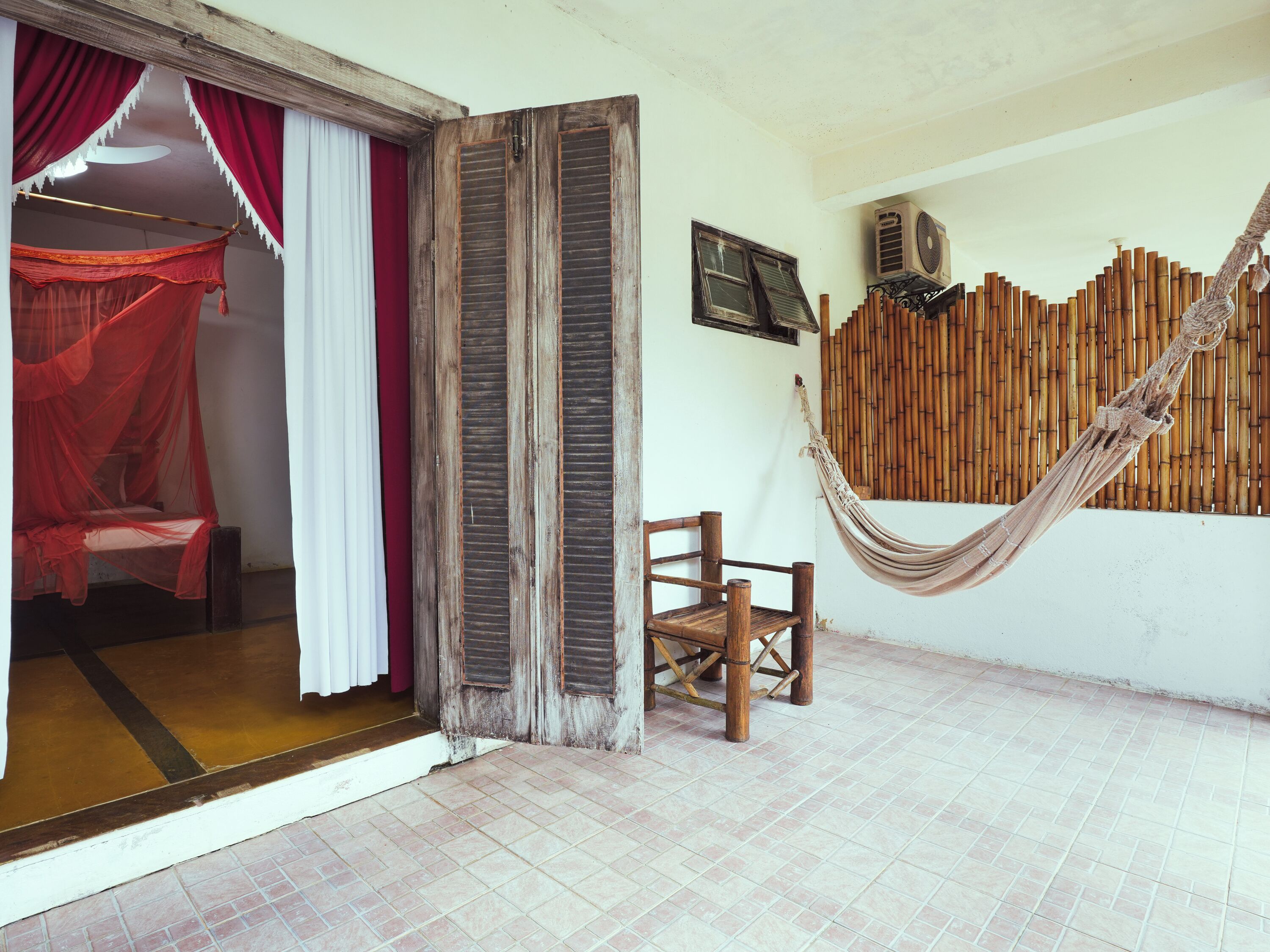 A room with a bed, a chair, a hammock, and a wall with a bamboo fence.