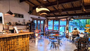 A restaurant with a bamboo wall, multiple tables, and hanging lights. - VELINN Pousada Bali Itamambuca (Ubatuba)