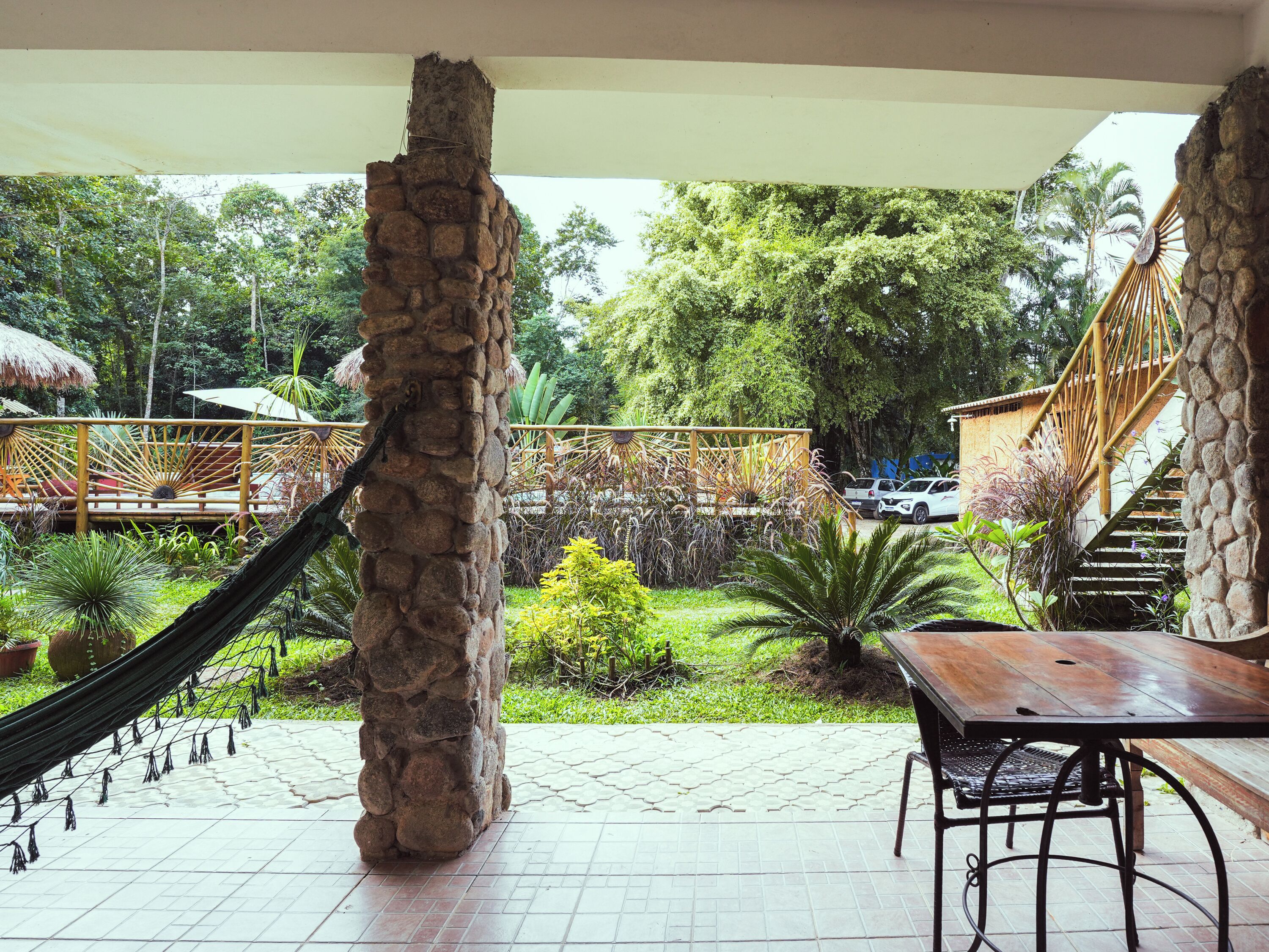 Un patio con un pilar de piedra, una hamaca, una mesa de madera y una escalera.
