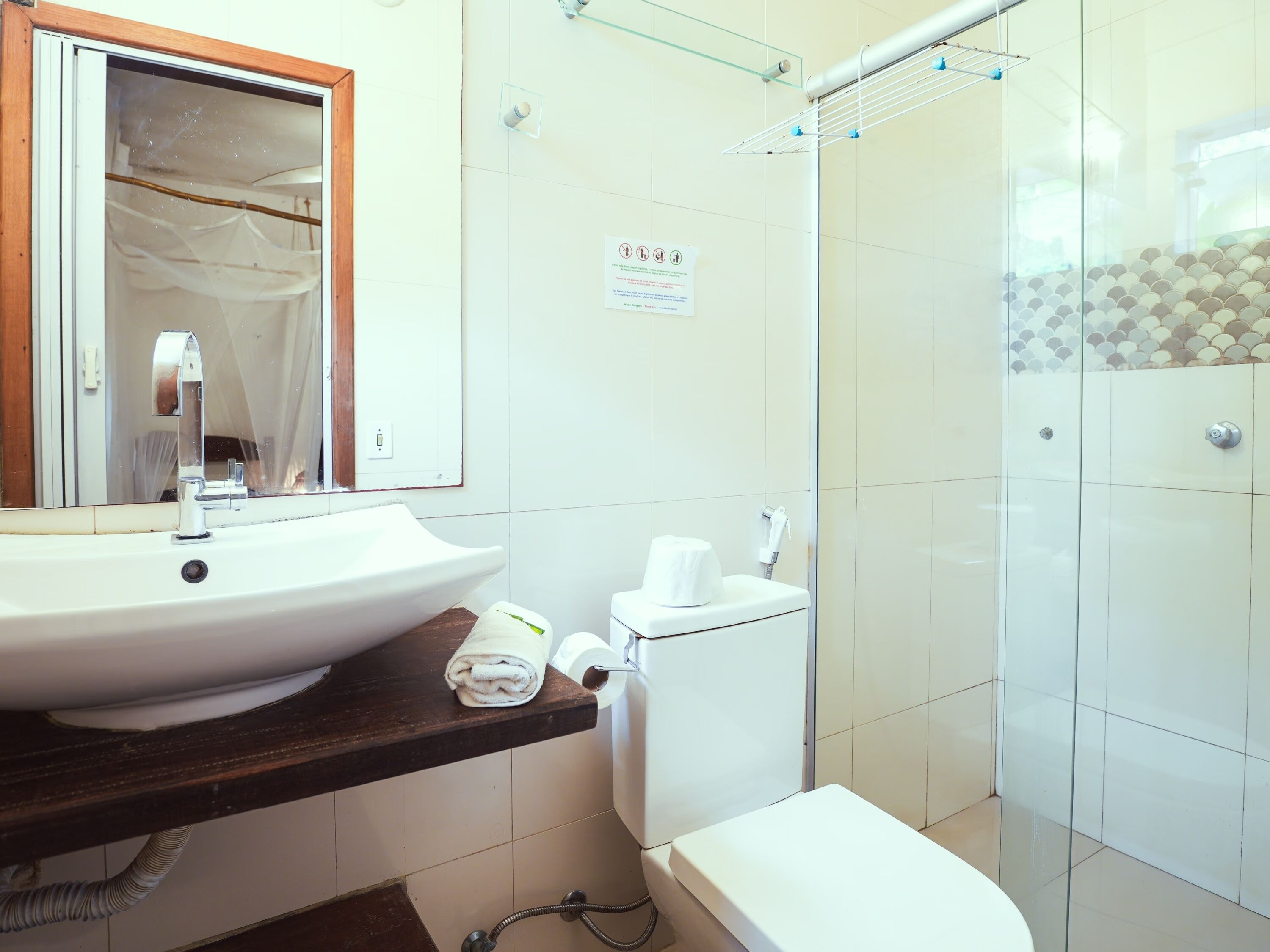 A bathroom with a white sink, toilet, and shower. There is a towel on the counter and a sign on the wall.