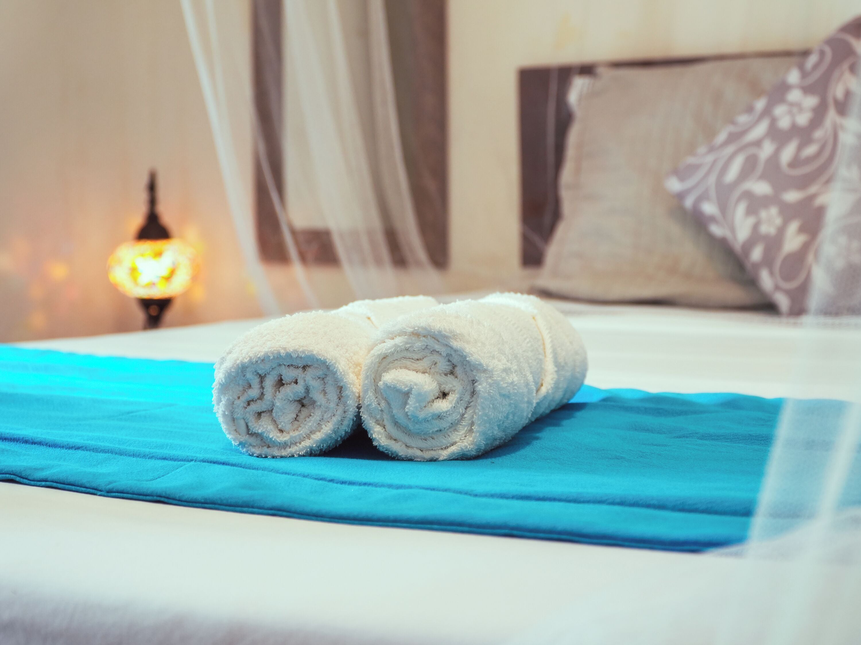 Una cama bien hecha con una colcha azul y dos toallas blancas enrolladas.