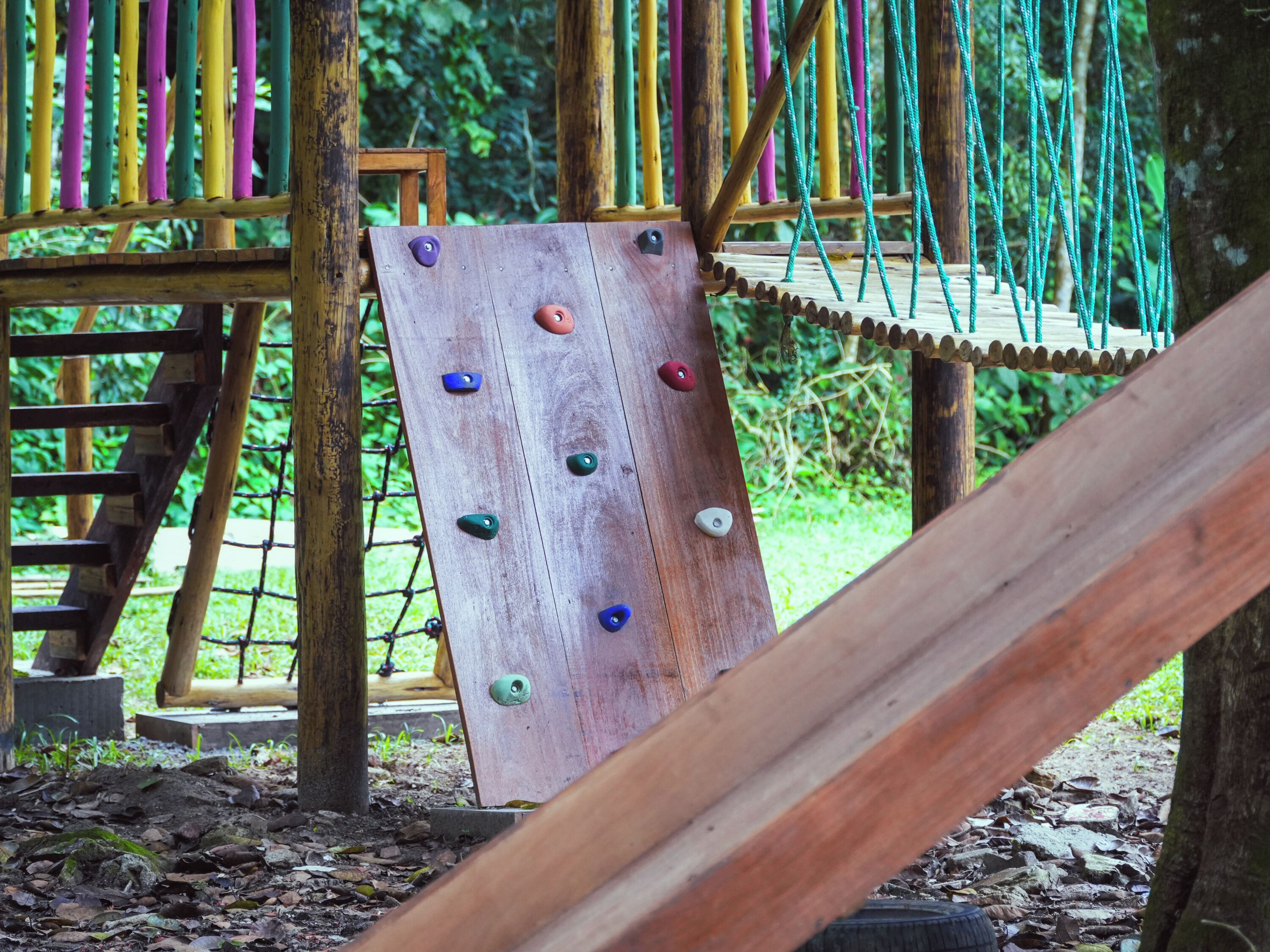 A wooden climbing structure with colorful holds and a rope netting.