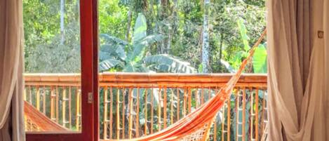 A hammock on a wooden deck with a view of a tropical forest.