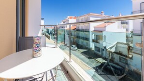A balcony with a glass railing overlooking a street with buildings. - Aris Apartment, Vila Nova de Cacela, Algarve (Vila Nova de Cacela)