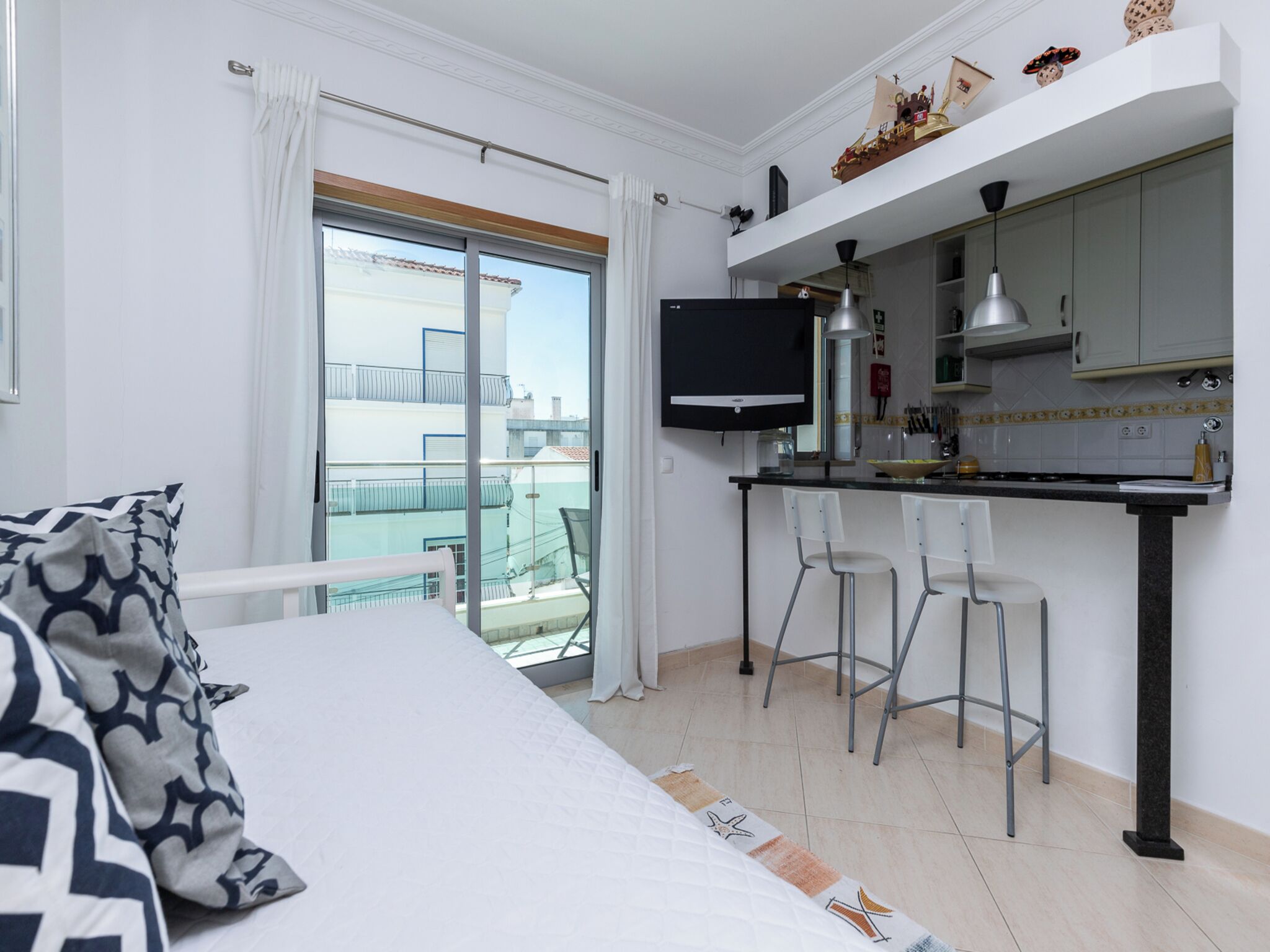 Ein Schlafzimmer mit Bett, Balkon mit Blick, einer Küchenzeile mit Fernseher und einem Essbereich mit Stühlen.