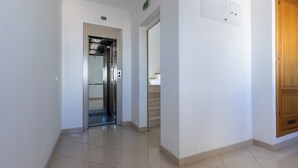 A clean, modern hallway with a shiny tiled floor, a wooden door, and a visible elevator. - Aris Apartment, Vila Nova de Cacela, Algarve (Vila Nova de Cacela)