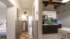 Μια μικρή, λειτουργική κουζίνα με σύγχρονες ηλεκτρικές συσκευές, μια τραπεζαρία με ένα λευκό τραπέζι και καρέκλες και ένα δάπεδο με καρό σχέδιο.
