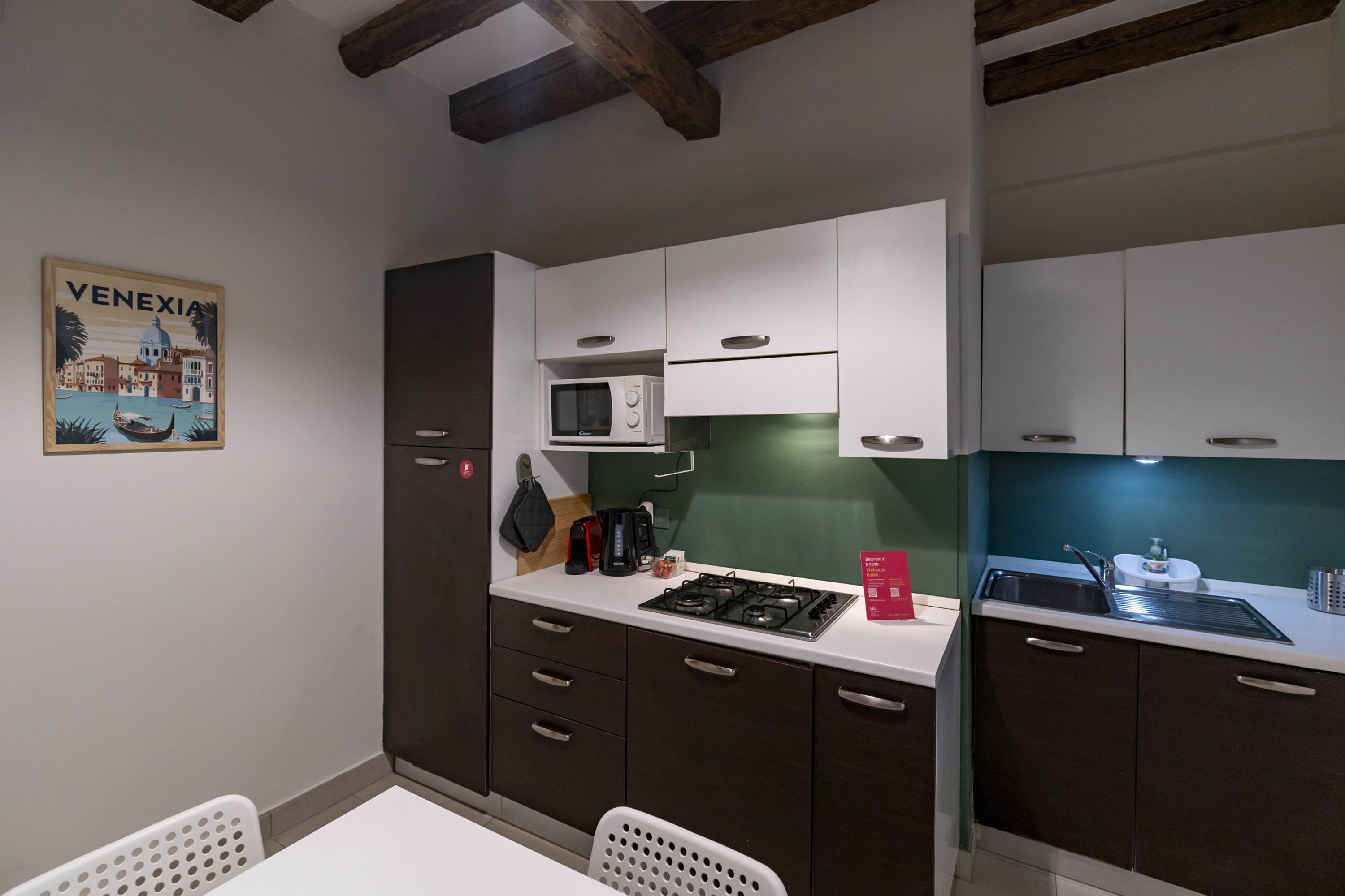A compact kitchen with white and dark brown cabinets, a microwave, a gas stove, and a sink.