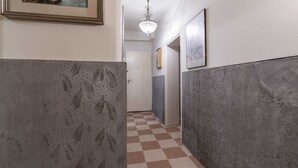 Ένας διάδρομος με διακοσμημένους τοίχους, ένα δάπεδο με καρό σχέδιο, ένα πολυέλαιο και έργα τέχνης σε κορνίζες.