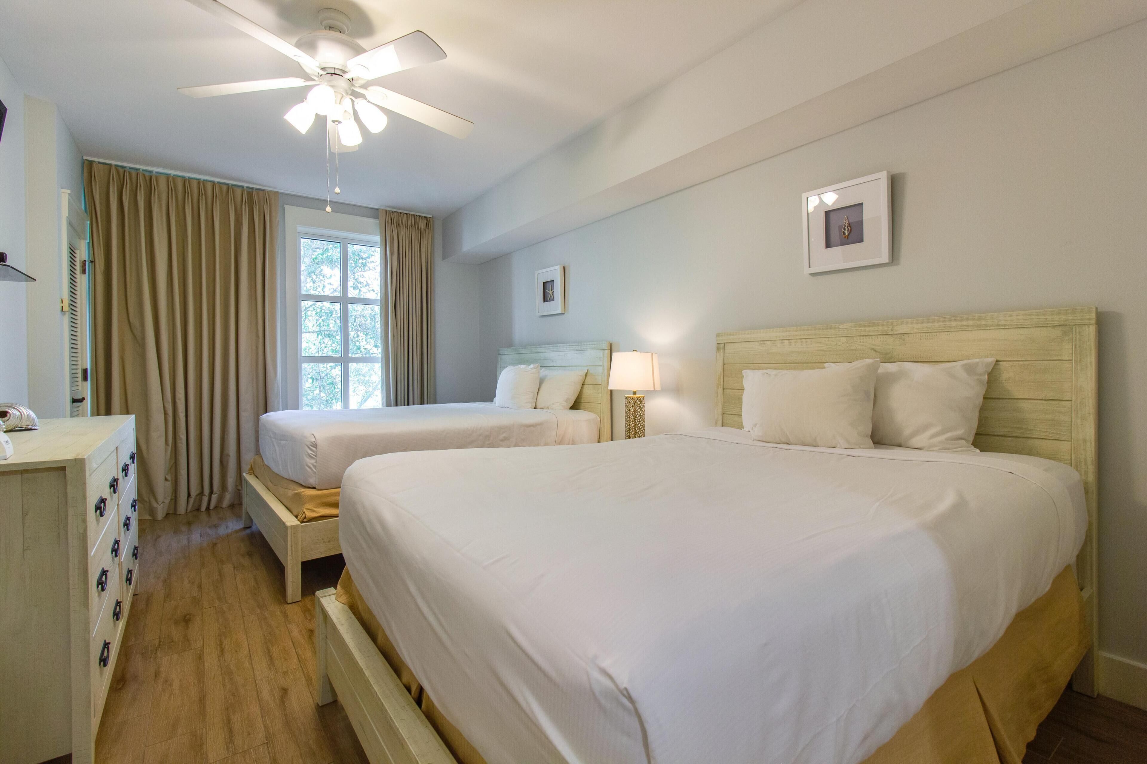 Une chambre d’hôtel avec deux lits, un ventilateur de plafond, une fenêtre avec des rideaux et une commode.