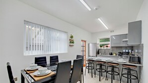 Una cocina moderna con comedor, que cuenta con un gran ventanal, paredes blancas y una barra con taburetes.