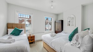 Habitación de hotel con dos camas individuales, cabecero de madera, armario y vistas al exterior a través de amplias ventanas.