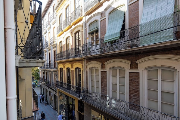 Un edificio de varios pisos con balcones, ventanas amplias y una calle estrecha.