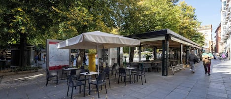An outdoor café with tables and chairs, surrounded by trees and buildings.