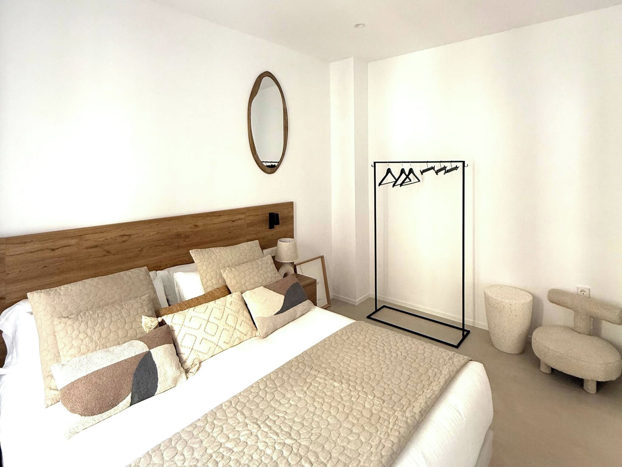 A modern bedroom with a large bed, a wooden headboard, a mirror, a wardrobe, and a seating area.