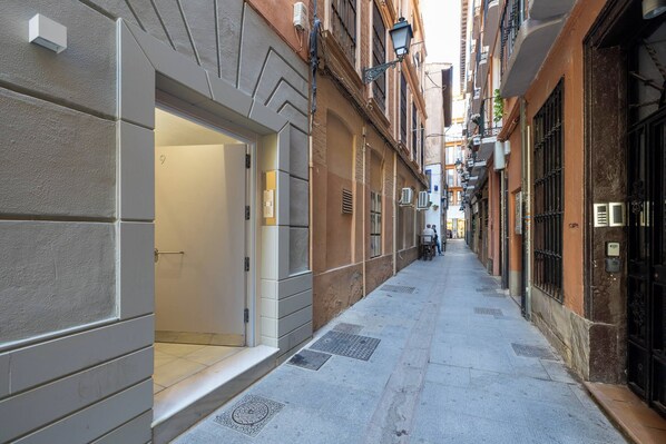 A narrow alleyway with a building entrance, a door, and a small outdoor seating area.