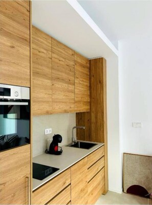 A modern kitchen with wooden cabinets, a built-in oven, a sink, and a black coffee maker.