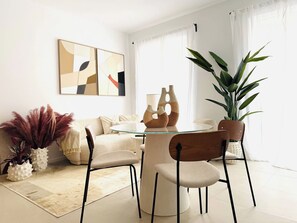 Una sala de estar moderna con una mesa redonda de vidrio, dos sillas, un sofá, una mesita de centro y jarrones decorativos.