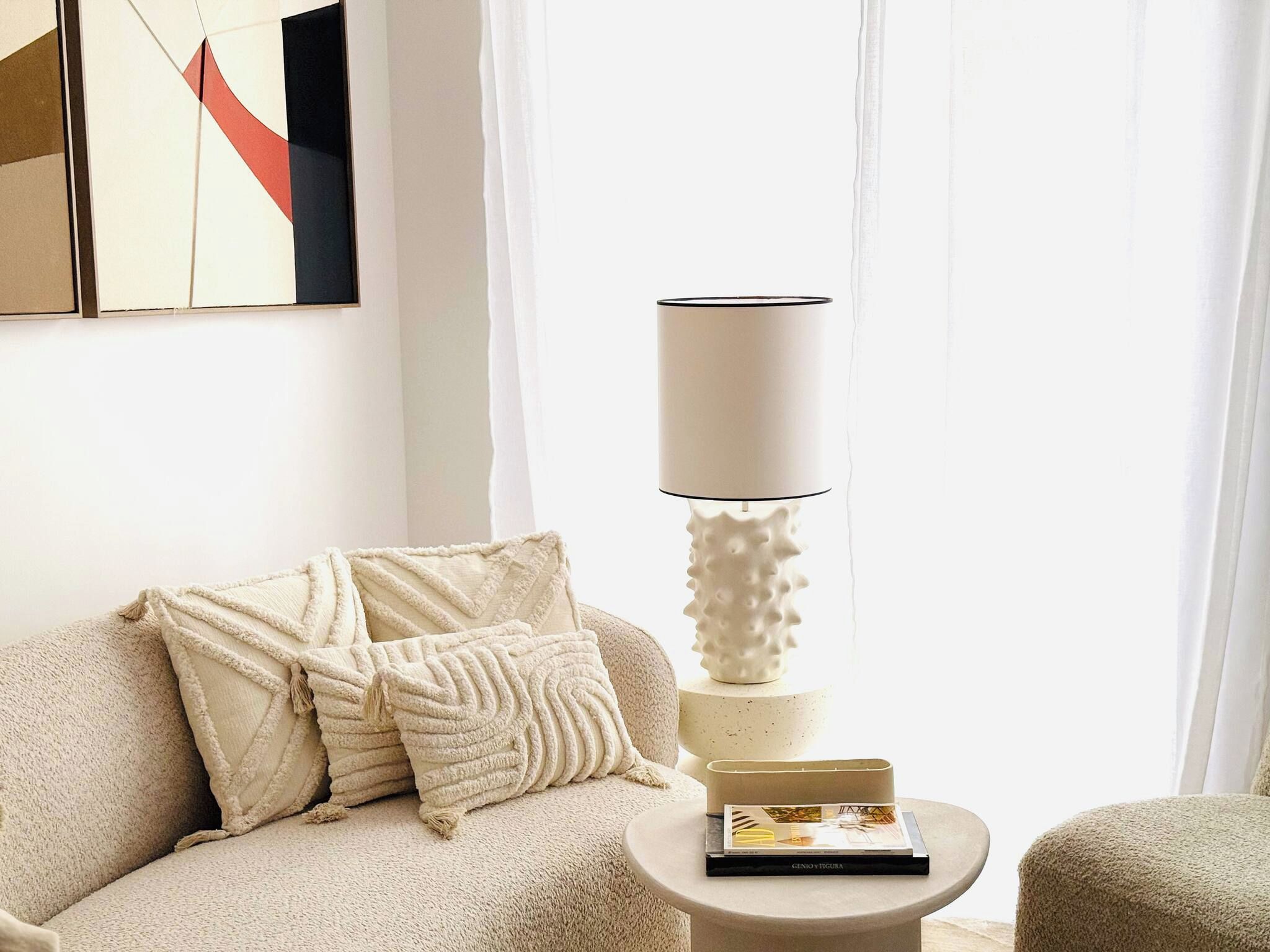 A living room with a sofa, pillows, a lamp, and a small table with a book.