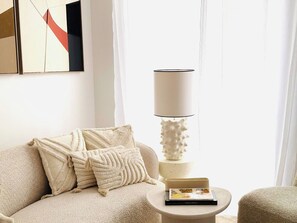 Ein Wohnzimmer mit einer Couch, Kissen, einer Lampe und einem kleinen Tisch mit einem Buch.
