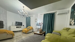 Una sala de estar moderna con un sofá, un televisor, una araña y un jarrón decorativo.