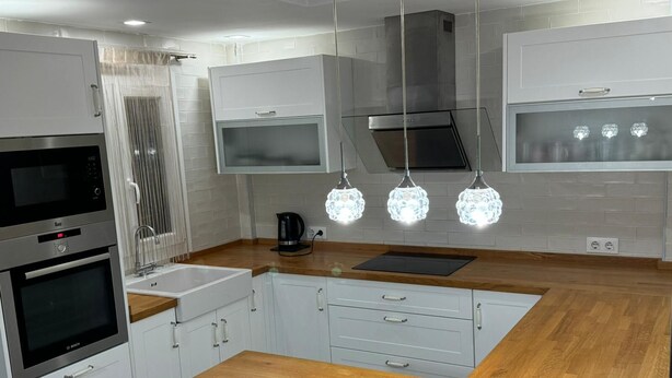 Una cocina moderna con armarios blancos, electrodomésticos de acero inoxidable y encimera de madera.