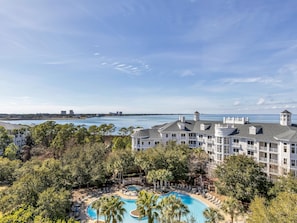 A resort with a large pool surrounded by palm trees and a view of the ocean. - Eighth floor in Grand Sandestin 1BR & 2BA with Bay & Pool views at Sandestin Golf & Beach Resort! (Miramar Beach)