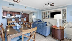 A spacious living area with a dining table, blue sofa, and a TV.