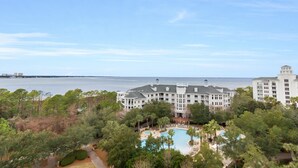 A large resort with a pool, surrounded by trees and overlooking a body of water.