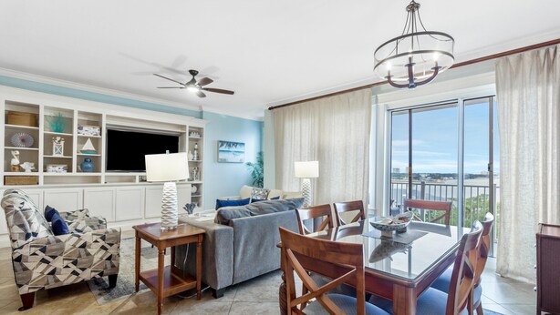 A living room with a sofa, a dining table with chairs, a TV, and a balcony with a view.