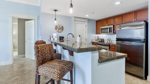 A modern kitchen with a central island, stainless steel appliances, and a seating area with woven chairs.