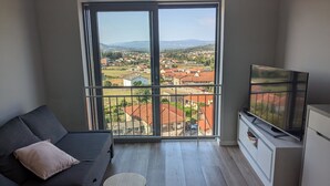 A modern living room with a grey sofa, a TV on a stand, and a balcony with a city view. - Accommodation in house with shared pool, 10mn from Braga. Weekly rental (BRAGA)
