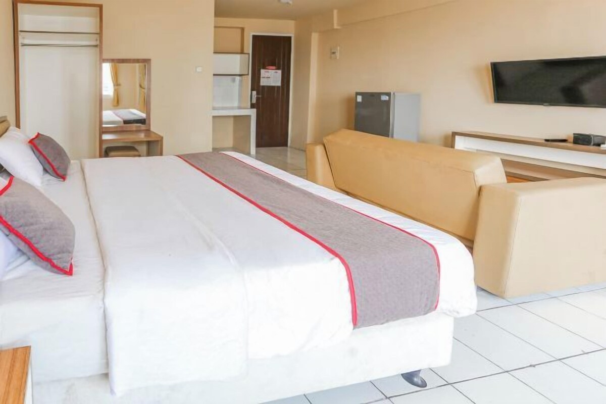 A hotel room with a large bed, a sofa, a TV, and a small kitchenette.