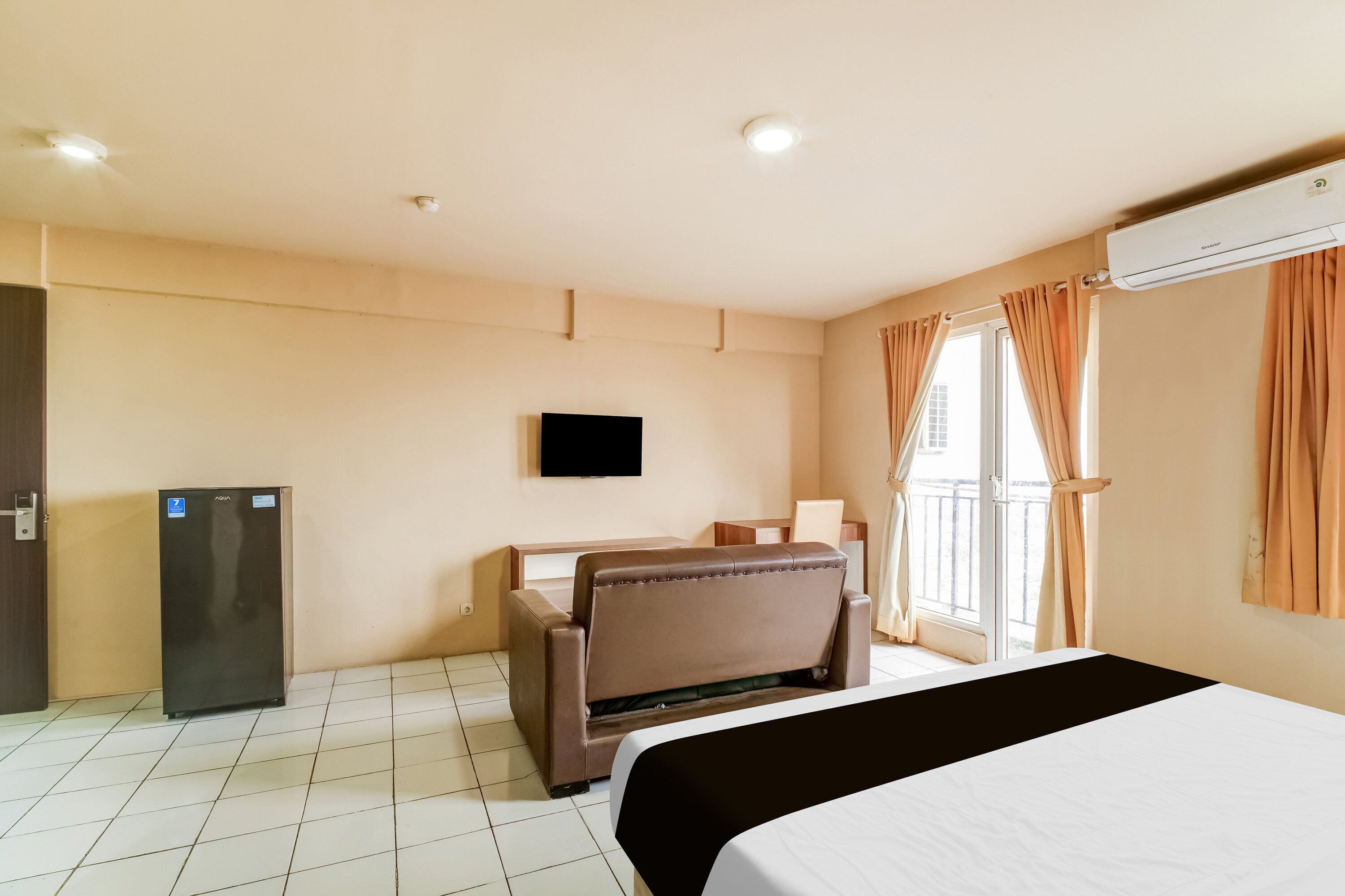 A hotel room with a bed, a desk, a chair, a television, and an air conditioning unit.