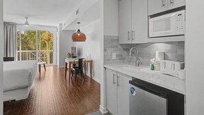 A modern kitchen with white cabinets, a microwave, and a dishwasher. There is a dining area with a table and chairs, and a balcony with a view of trees. - Elation 2BR: Sunset Views & Steps to Baytowne (Miramar Beach)